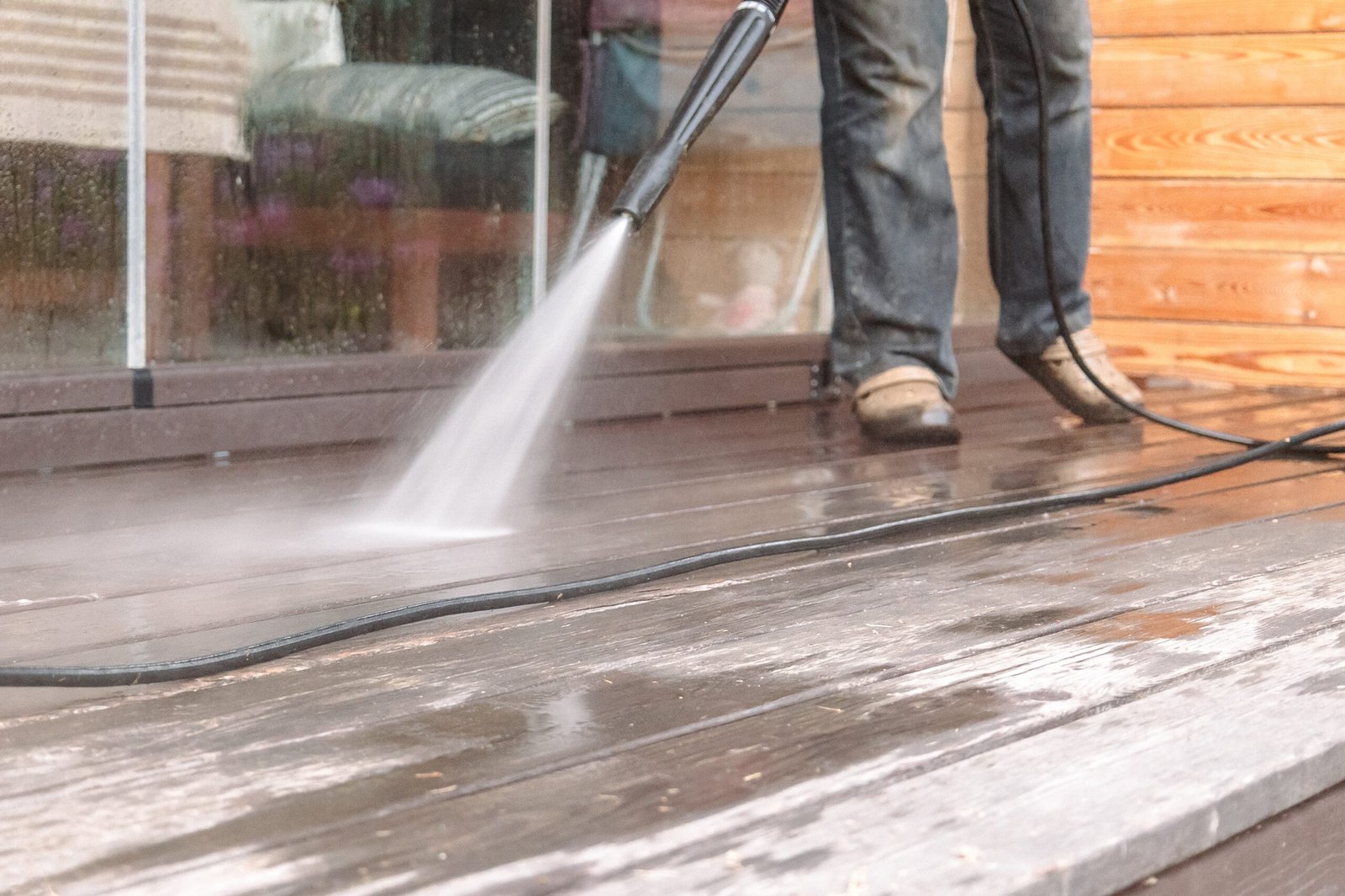 A man performing pressure washing services on a wooden deck