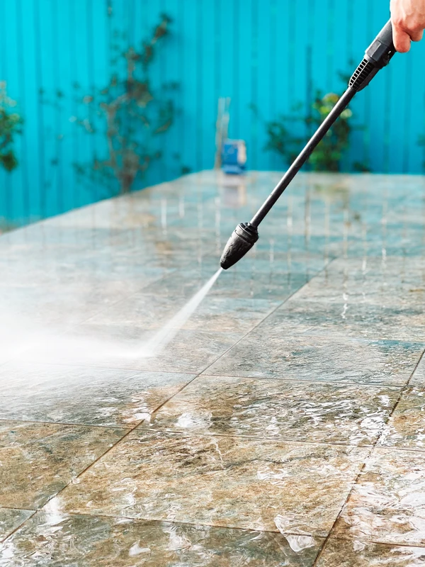 Pressure washing gun being used to blast away dirt on a concrete patio
